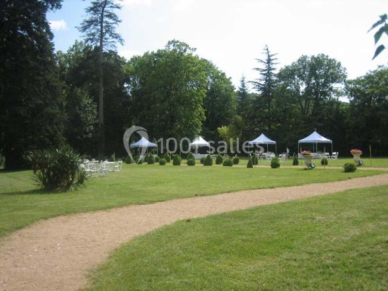 Pelouse avec chemin en gravier, tentes blanches et mobilier de jardin entourés d'arbres et de verdure.