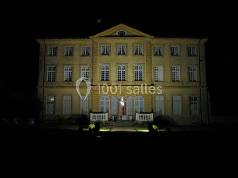 Façade d'un grand bâtiment ancien éclairé la nuit, avec des fenêtres symétriques et une porte centrale illuminée.