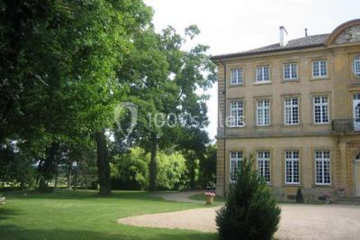 Chambre ancienne avec lit à baldaquin, fauteuil rouge, cheminée noire et murs tapissés de motifs verts.