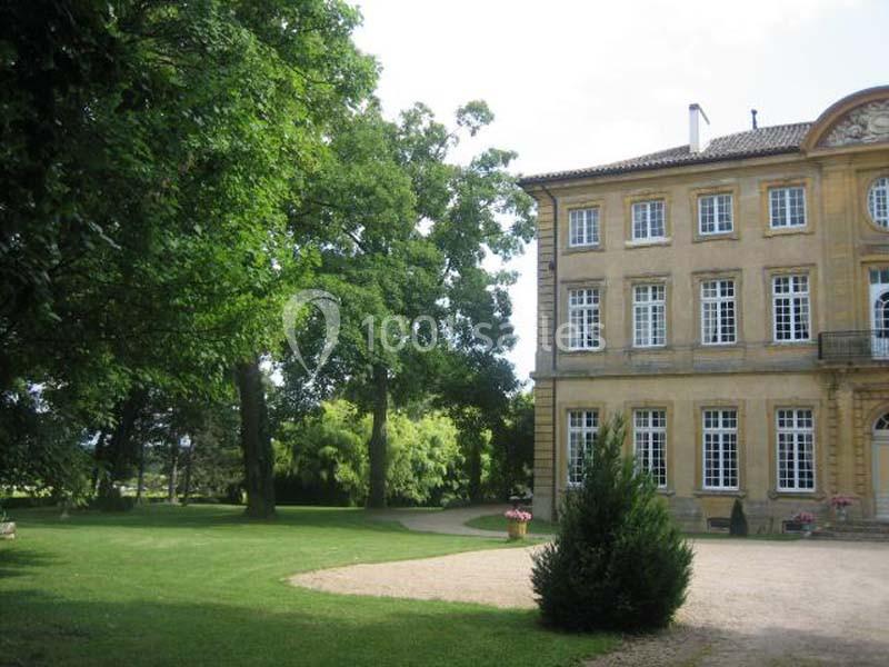 Façade d'un bâtiment ancien en pierre, entouré d'arbres et d'une pelouse avec une allée gravillonnée.