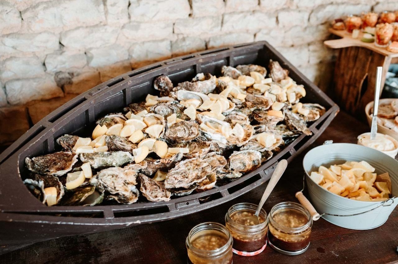 Plateau d'huîtres avec quartiers de citron dans un contenant en forme de bateau, accompagné de sauces et condiments.