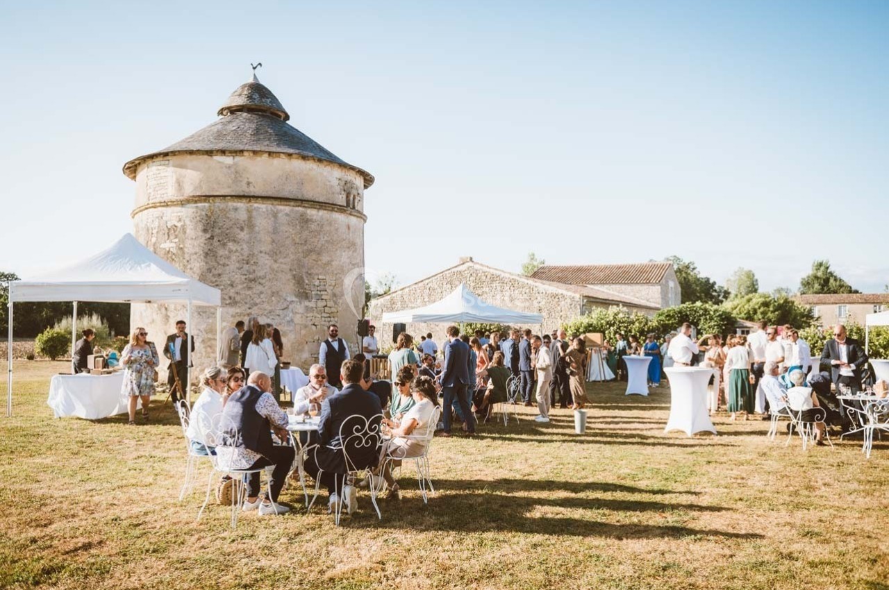 Groupe de personnes réunies en extérieur lors d'un événement, avec des tables, des tentes et un bâtiment en pierre en…