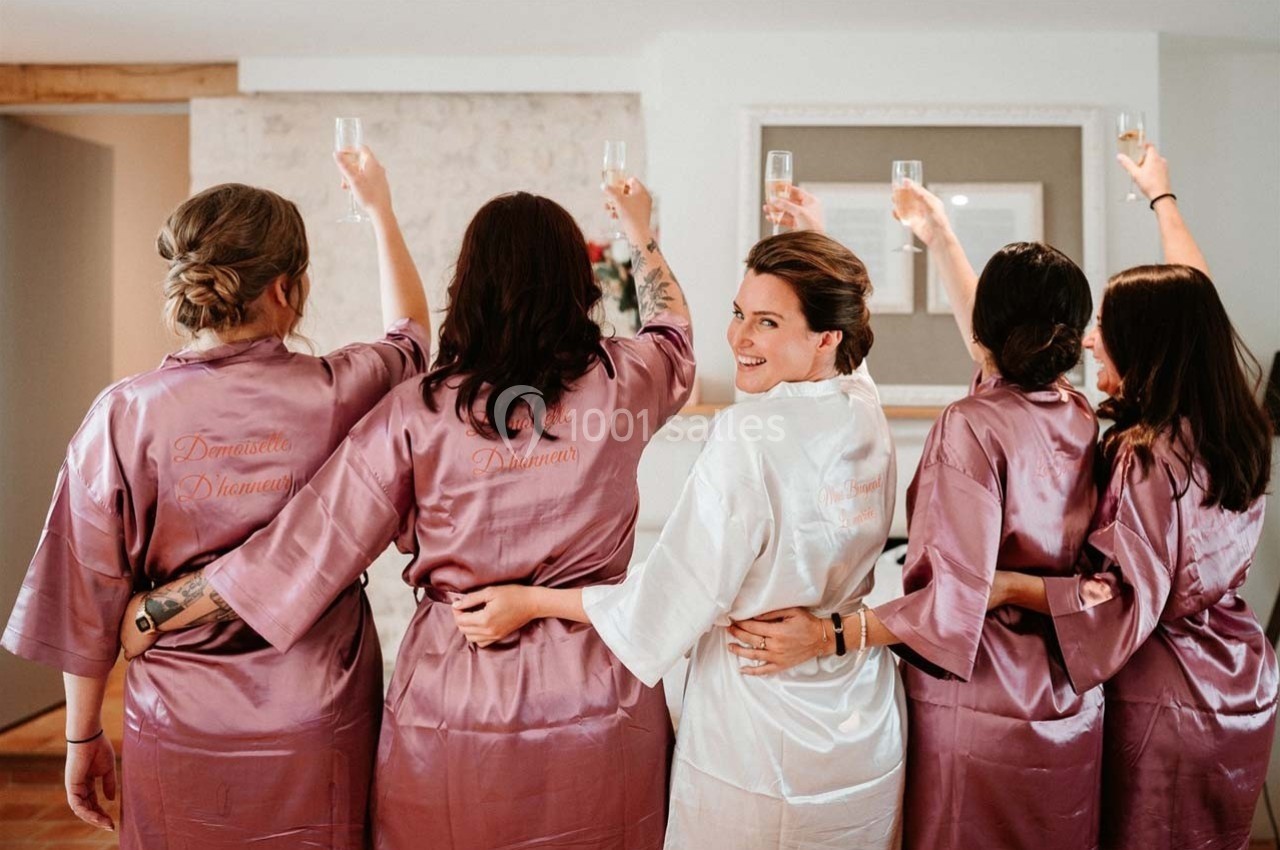 Cinq femmes en peignoirs, levant des verres de champagne, dans une ambiance festive et détendue.