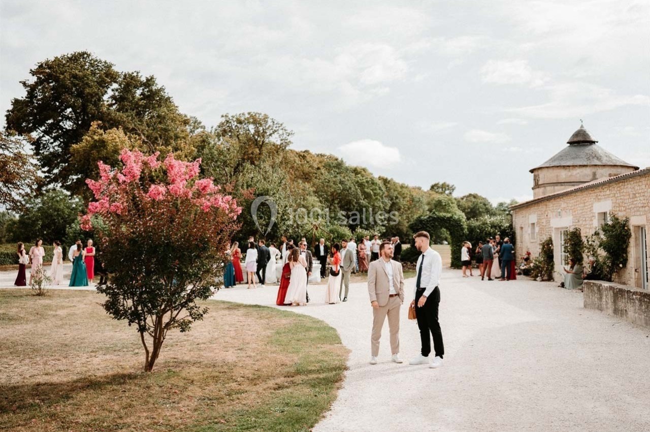 Groupe de personnes rassemblées dans une cour extérieure près d'un bâtiment en pierre, avec un arbre en fleurs au premier…