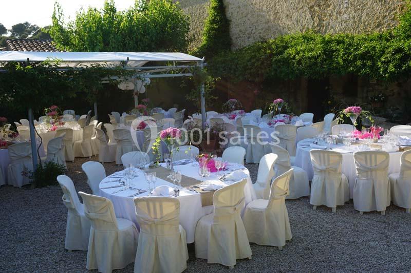 Tables rondes décorées pour un événement en extérieur, entourées de chaises blanches et de verdure.