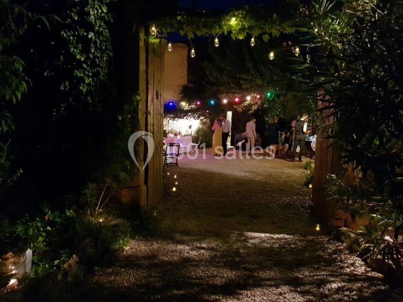 Cour extérieure éclairée par des guirlandes lumineuses colorées, avec des invités debout et discutant en soirée.