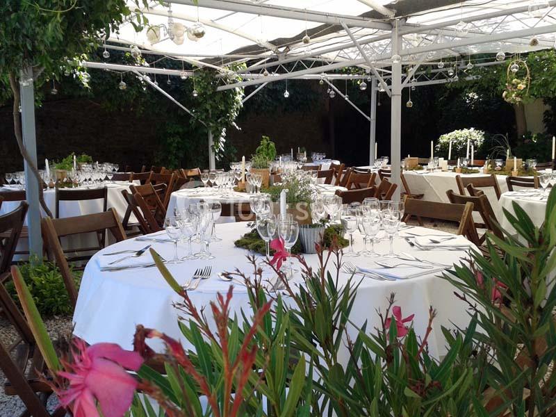 Tables rondes élégamment dressées sous une pergola blanche, entourées de verdure et de fleurs.