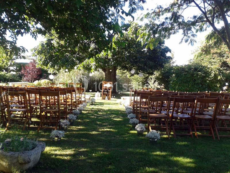 Chaises en bois disposées en rangées face à une table sous un grand arbre, décorées pour une cérémonie en extérieur.