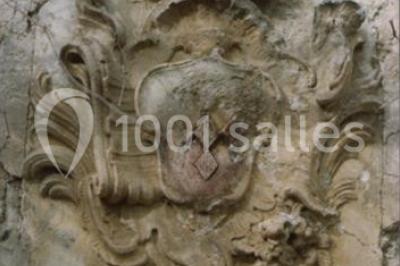 Blason sculpté en pierre, usé par le temps, fixé sur un mur ancien avec des branches visibles au-dessus.