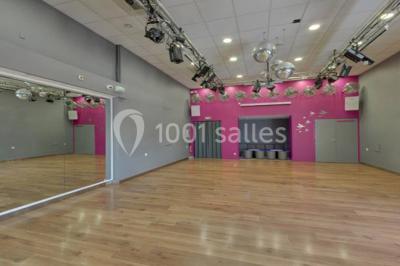 Salle de danse vide avec éclairage coloré, boules à facettes suspendues et reflets lumineux sur les murs.