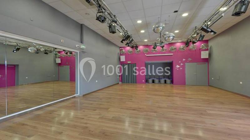 Salle de danse avec parquet, miroirs sur un mur, éclairages suspendus et murs gris et rose.