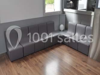 Canapé d'angle modulable gris sur un sol en parquet, placé dans un coin de pièce lumineuse avec une fenêtre.