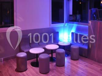 Banquettes grises, tabourets et tables rondes dans une pièce éclairée par une lumière bleue.