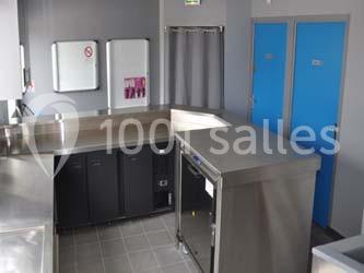 Cuisine professionnelle avec plans de travail en inox, armoires de rangement, et portes bleues en arrière-plan.