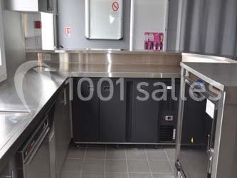 Cuisine professionnelle avec équipements en inox, plan de travail, armoires réfrigérées et sol carrelé gris.