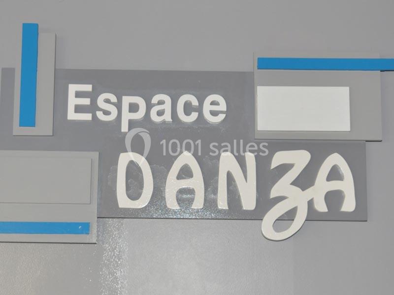 Enseigne murale grise avec le texte ’Espace Danza’ en lettres blanches, entourée de formes géométriques.