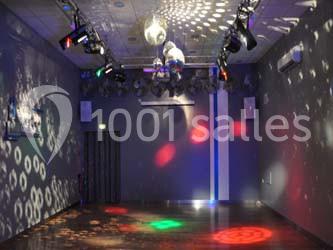 Salle de danse vide avec éclairage coloré, boules à facettes suspendues et reflets lumineux sur les murs.