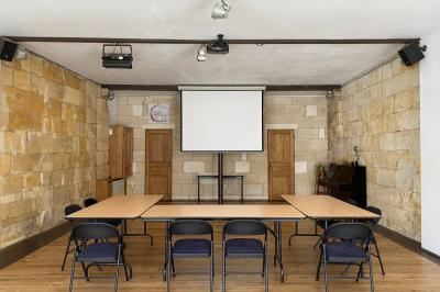 Salle lumineuse avec parquet en bois, murs clairs, chaises noires alignées et grande baie vitrée en arrière-plan.