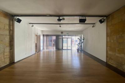 Salle lumineuse avec parquet en bois, murs clairs, chaises noires alignées et grande baie vitrée en arrière-plan.