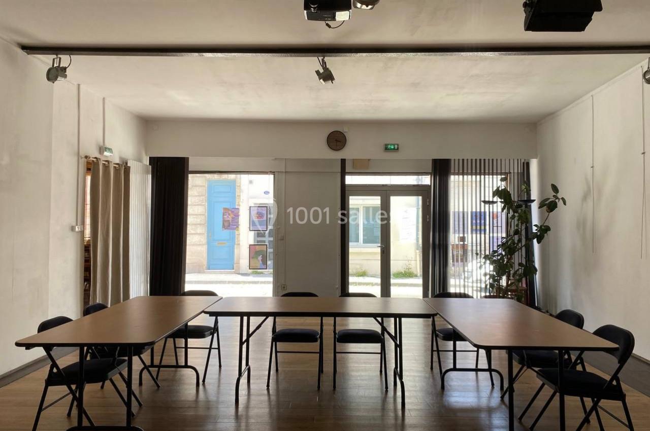 Salle lumineuse avec tables et chaises disposées en rectangle, grandes baies vitrées donnant sur une cour extérieure.