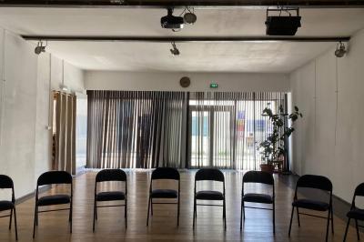 Salle lumineuse avec parquet en bois, murs clairs, chaises noires alignées et grande baie vitrée en arrière-plan.