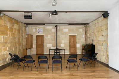 Salle lumineuse avec parquet en bois, murs clairs, chaises noires alignées et grande baie vitrée en arrière-plan.