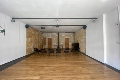 Salle lumineuse avec parquet en bois, murs clairs, chaises noires alignées et grande baie vitrée en arrière-plan.