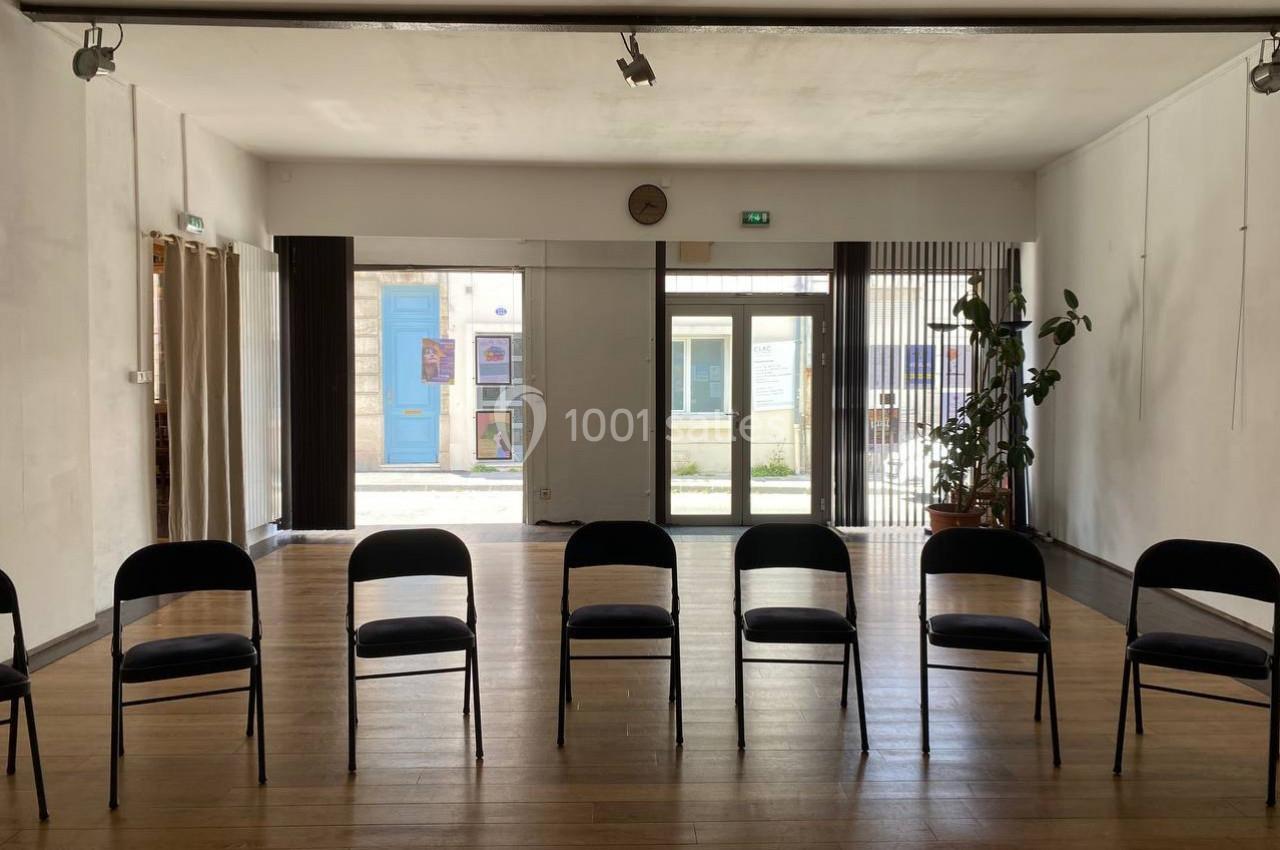 Salle lumineuse avec parquet, rangée de chaises noires alignées face à des baies vitrées donnant sur une cour extérieure.