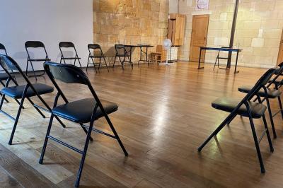 Salle lumineuse avec parquet en bois, murs clairs, chaises noires alignées et grande baie vitrée en arrière-plan.