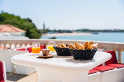 Repas avec poisson, burger, vin et eau servis sur une table en terrasse avec vue sur la mer.