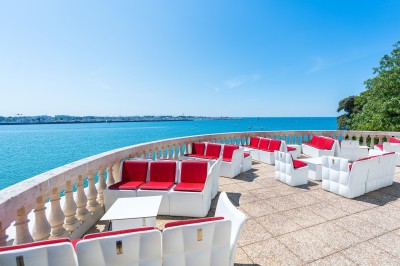 Repas avec poisson, burger, vin et eau servis sur une table en terrasse avec vue sur la mer.