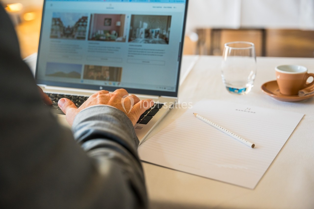 Une personne utilise un ordinateur portable sur une table avec un carnet, un crayon, un verre d'eau et une tasse de café.