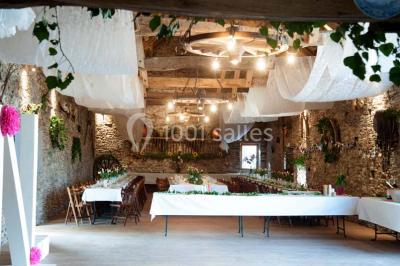 Tables décorées de nappes blanches, ornées de bougies entourées de fleurs, dans un cadre extérieur fleuri.