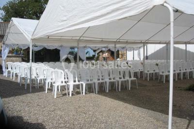 Tables décorées de nappes blanches, ornées de bougies entourées de fleurs, dans un cadre extérieur fleuri.