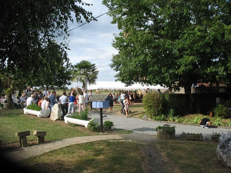 Groupe de personnes rassemblées en extérieur dans un jardin avec arbres, pelouse et ciel partiellement nuageux.