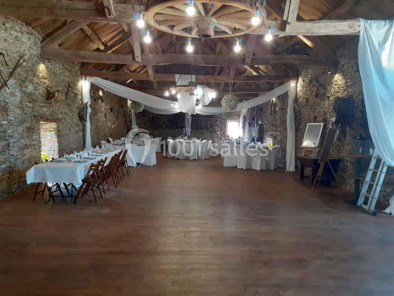 Salle de réception rustique avec murs en pierre, poutres apparentes et tables dressées pour un événement.