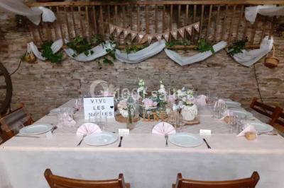 Tables décorées de nappes blanches, ornées de bougies entourées de fleurs, dans un cadre extérieur fleuri.