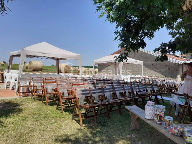 Chaises en bois disposées sous des tonnelles blanches dans un espace extérieur, avec des bottes de foin en arrière-plan.