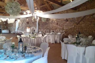 Tables décorées de nappes blanches, ornées de bougies entourées de fleurs, dans un cadre extérieur fleuri.