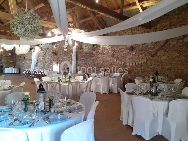 Salle de réception décorée avec des tables rondes dressées, des nappes blanches et des guirlandes suspendues.