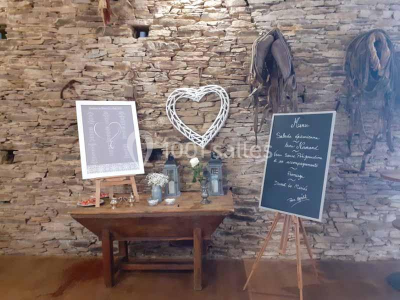 Table en bois décorée avec des fleurs, des lanternes et des tableaux, devant un mur en pierre avec un cœur en osier.