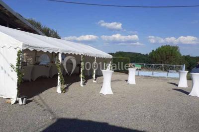 Tables décorées de nappes blanches, ornées de bougies entourées de fleurs, dans un cadre extérieur fleuri.