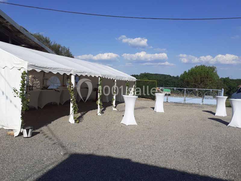 Tente blanche installée en extérieur sur un sol gravillonné, avec des tables hautes recouvertes de housses blanches.