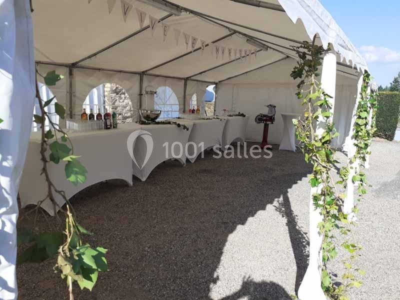 Tente blanche aménagée avec des tables drapées, décorée de guirlandes de lierre, pour un événement en extérieur.