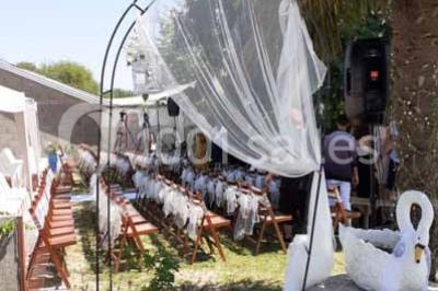 Tables décorées de nappes blanches, ornées de bougies entourées de fleurs, dans un cadre extérieur fleuri.