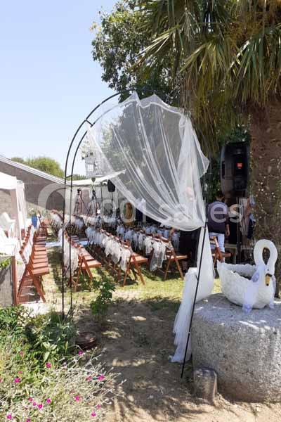 Arche décorée de voilage blanc dans un jardin, entourée de chaises en bois alignées pour une cérémonie en plein air.