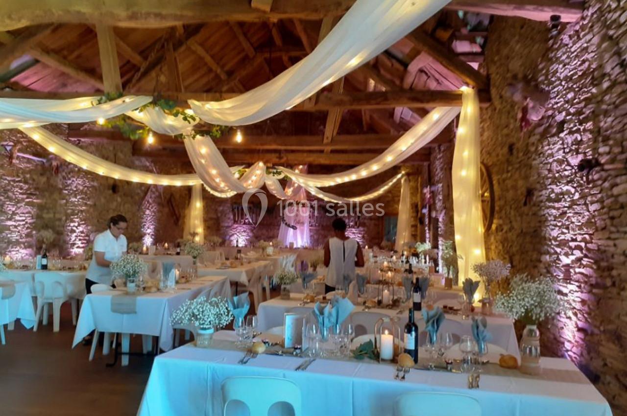 Salle de réception rustique décorée de guirlandes lumineuses, nappes blanches et compositions florales.