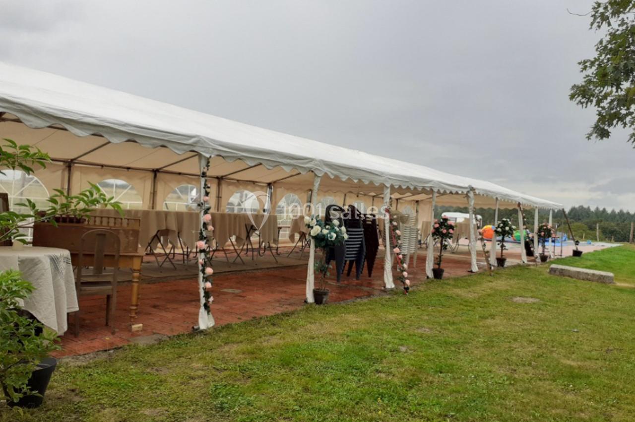 Grande tente blanche installée sur une pelouse, décorée de fleurs, avec tables et chaises pour un événement en extérieur.