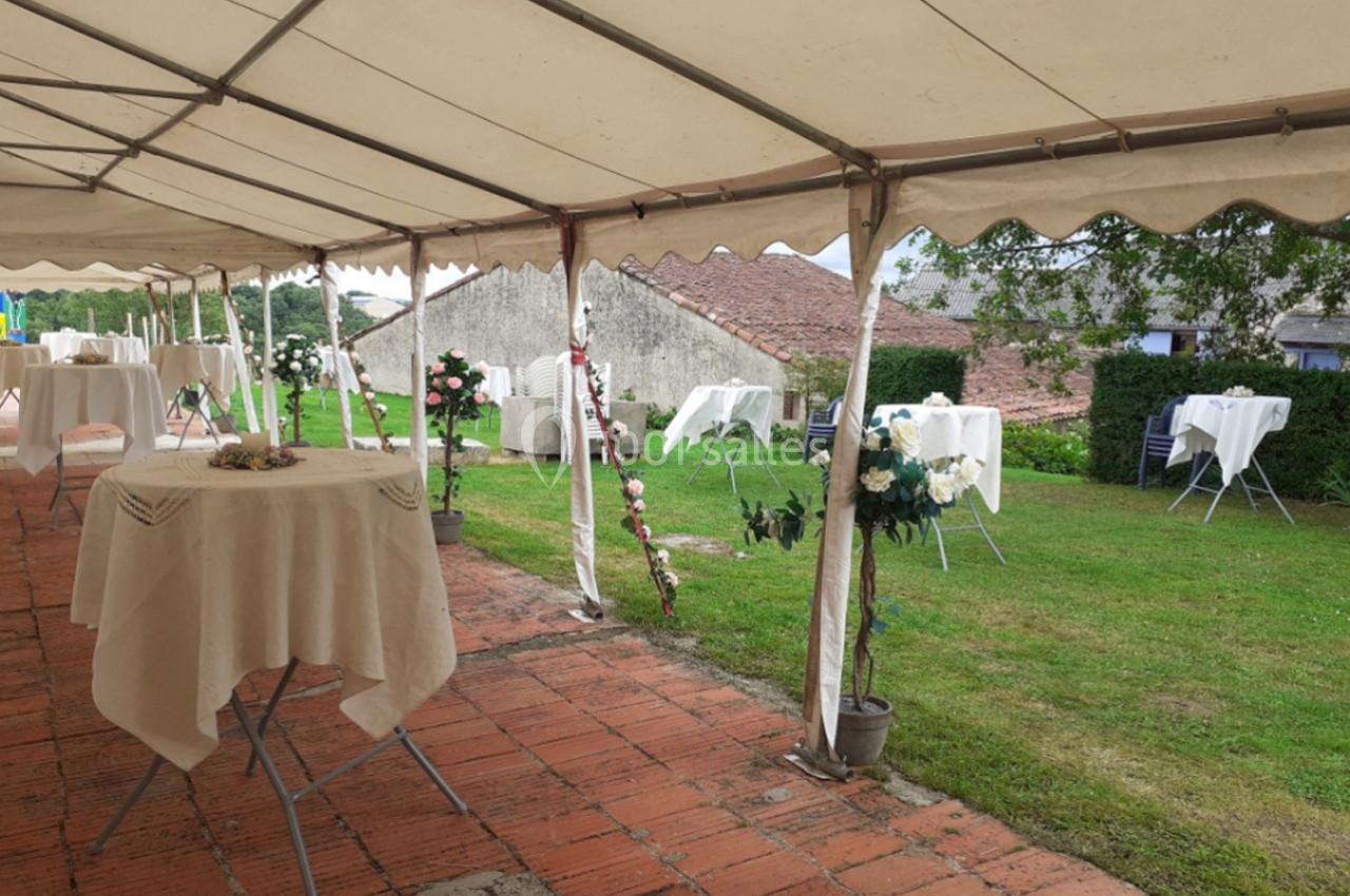 Tente blanche avec tables dressées sur une terrasse en briques, donnant sur un jardin verdoyant.