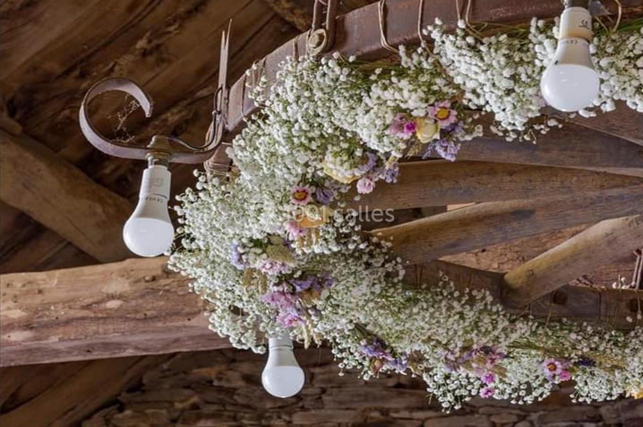 Couronne florale suspendue avec des gypsophiles et des fleurs colorées, décorée d'ampoules, sur fond de poutres en bois.